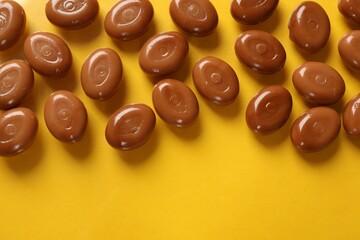 Many tasty caramel candies on yellow background, flat lay. Space for text
