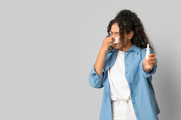 Young African-American woman with handkerchief and nasal spray suffering from allergy on white...