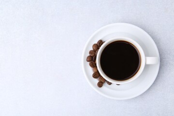 Aromatic coffee in cup, beans and saucer on light table, top view. Space for text