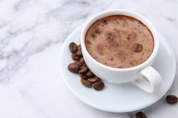 Aromatic coffee in cup, beans and saucer on white marble table, closeup. Space for text