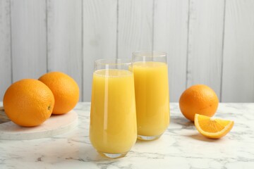 Orange juice in glasses and fresh fruits on white marble table