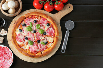 Tasty pizza, ingredients and cutter on black wooden table, flat lay. Space for text