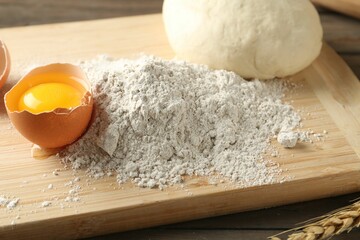 Pile of flour, broken egg and dough on wooden table, closeup