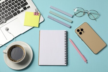 Notebook, other stationery, smartphone, coffee, glasses, earphones and laptop on light blue background, flat lay