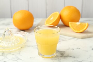 Fresh orange juice, fruits and squeezer on white marble table, closeup