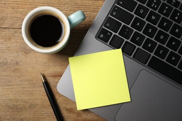 Laptop with sticky note, pen and coffee on wooden table, top view