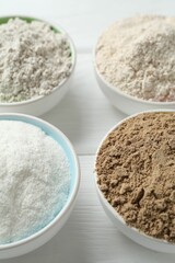 Different types of flour in bowls on white wooden table, closeup
