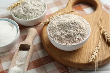 Different types of flour in bowls, scoop and spikes on table, closeup
