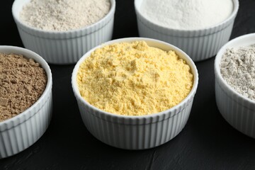 Different types of flour in bowls on black table, closeup