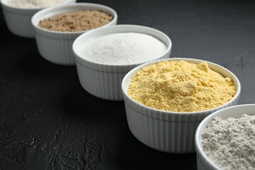 Different types of flour in bowls on black textured table, closeup