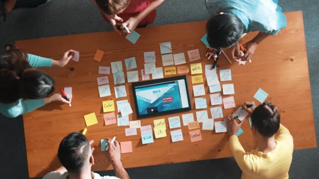 Top down view of programmer brainstorming and planning about web design while looking at tablet wireframe prototype. Aerial view of skilled developer team talking about digital application. Symposium.