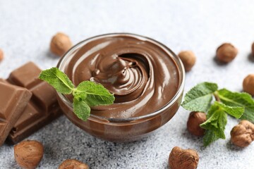 Tasty chocolate spread with mint in bowl and hazelnuts on grey textured table, closeup