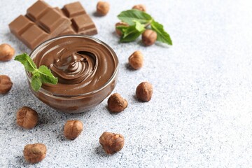 Tasty chocolate spread with mint in bowl and hazelnuts on grey textured table, closeup. Space for text