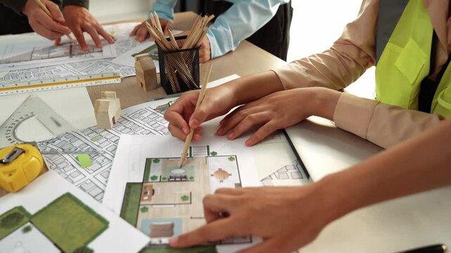 Smart architect and safety engineer discussion about building blueprint on table with architectural document, measurement tools and wooden block scatter around at modern office. Closeup. Delineation.