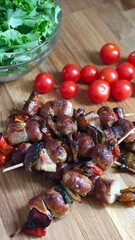 Savory skewers of grilled meats and vegetables alongside fresh cherry tomatoes and crisp greens on a wooden cutting board