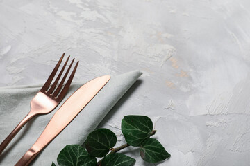 Stylish stainless cutlery and tree branch on grey background, closeup