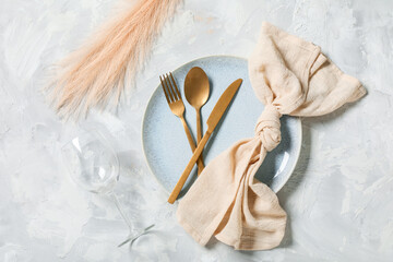 Beautiful table setting with golden cutlery and feathers on grey background