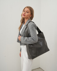 Stylish woman in a blazer and trousers poses with a chic bag in a minimalist setting