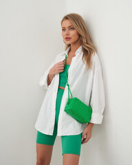 Young woman models vibrant green outfit paired with stylish bag in modern setting