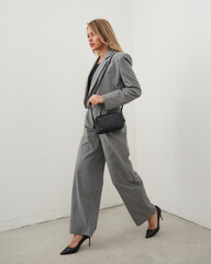Blonde woman confidently walking in a stylish gray suit with a clutch bag