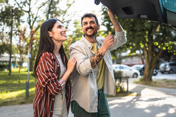 beautiful happy couple stand by the trunk and get ready to leave city