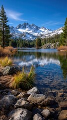 Scenic Alpine Lake reflects snow-covered mountain peaks and evergreen forest on a sunny day with rocky shores and crystal clear water.