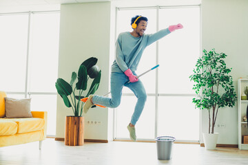 Young man in casual wear enjoying cleaning with a mop while dancing indoors in a modern and stylish living room