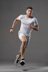 Handsome caucasian man running, wearing short sleeve shirt and shorts, sports running, fitness, gray background