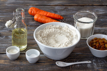 Set of ingredients for carrot cake on rustic wooden table: flour, sugar, carrots, raisins, oil. Home baking, cooking concept, natural ingredients