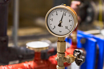 Close-up of a Brass Industrial Pressure Gauge Measuring in Bar, Connected to a Piping System.