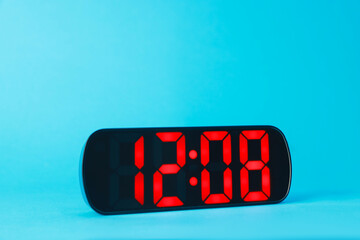 Digital alarm clock showing 12:08 o'clock on light blue background