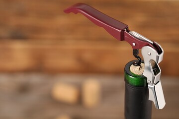 Bottle of luxury wine with corkscrew on blurred background, closeup. Space for text