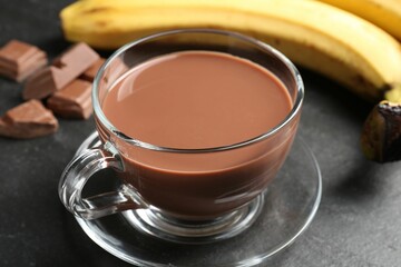 Tasty chocolate milk in glass cup, pieces and bananas on black table, closeup