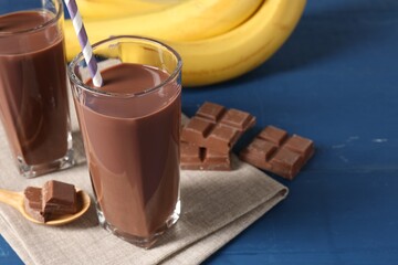 Tasty chocolate milk in glasses, pieces and bananas on blue wooden table, closeup. Space for text