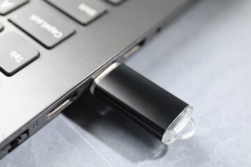 Flash drive connected to laptop on gray textured table, closeup