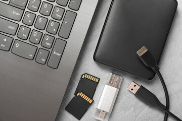 Flash drive, SD memory cards, external hard disk and laptop on gray textured table, flat lay