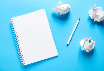 Open blank notebook, crumpled paper and pen on light blue background, flat lay