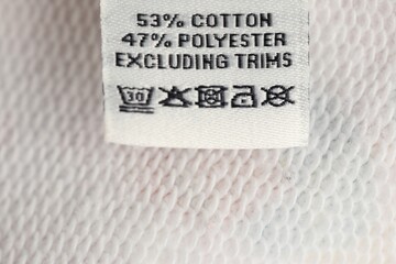 Clothing label on white garment as background, closeup