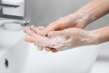Woman washing hands at sink in bathroom, closeup