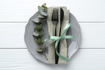 Stylish plate, napkin, cutlery and eucalyptus branch on white wooden table, top view