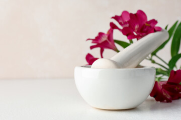 Ceramic mortar, pestle and flowers on white table, closeup. Space for text