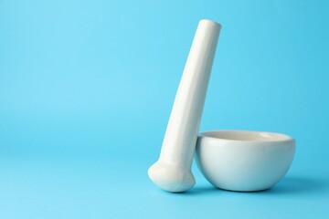 Ceramic mortar and pestle on light blue background, closeup. Space for text