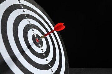 Targeting. Dart board with arrow on black background, closeup. Space for text
