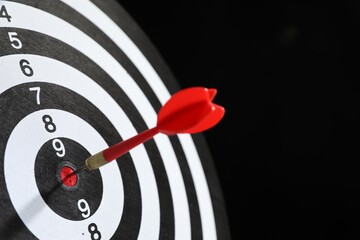 Targeting. Dart board with arrow on black background, closeup. Space for text