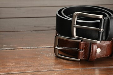 Two leather belts on wooden table, closeup. Space for text