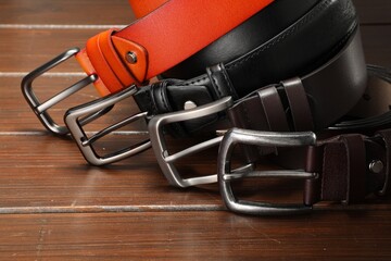 Many leather belts on wooden table, closeup