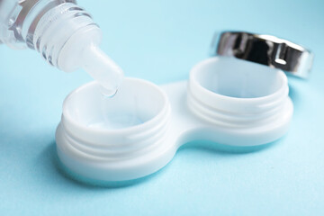 Dripping contact lens solution from bottle into case on light blue background, closeup