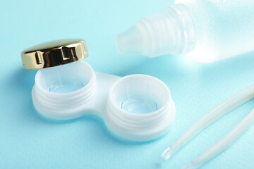 Contact lenses in case, solution and tweezers on light blue background, closeup