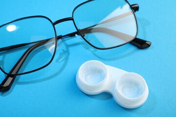Contact lenses in case and glasses on blue background, closeup