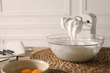 Hand mixer with whisks, bowl of whipped cream and yolks on table indoors, closeup
